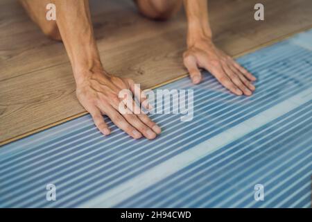 Uomo che installa nuovo pavimento in laminato di legno su un pavimento in pellicola calda. Impianto di riscaldamento a infrarossi sotto il pavimento in laminato Foto Stock