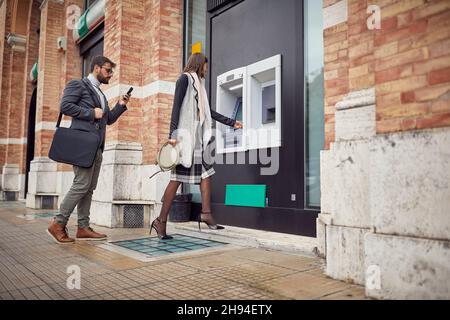 Uomini d'affari che ritirano il denaro presso l'ATM in città Foto Stock