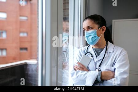 Dottore femminile che guarda fuori dalla finestra dell'ospedale Foto Stock