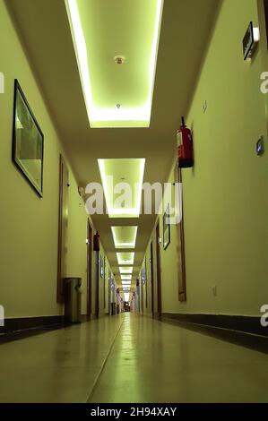 Corridoio illuminato dell'hotel con file di porte e dipinti sulle pareti che guardano in prospettiva Foto Stock