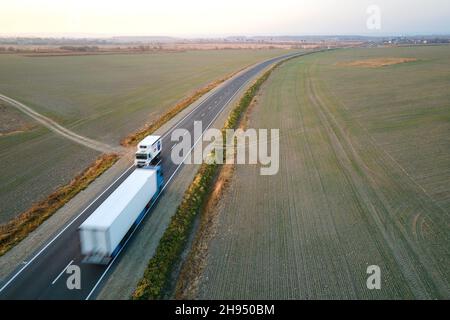 Vista aerea dei camion cargo che guidano su strade pubbliche che trasportano merci. Trasporto di consegna e concetto di logistica. Foto Stock
