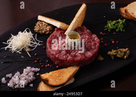 Tartare di manzo con uovo di quaglia e pane bianco tostato su un elegante piatto nero Foto Stock