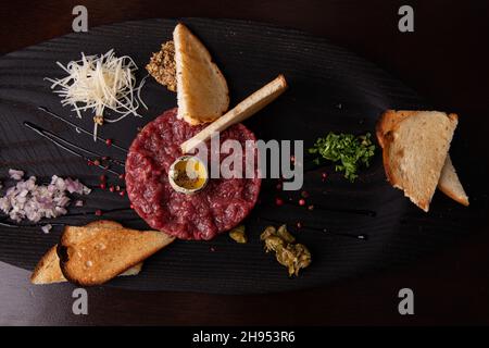 Tartare di manzo con uovo di quaglia e pane bianco tostato su un elegante piatto nero Foto Stock