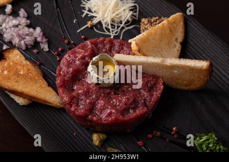 Tartare di manzo con uovo di quaglia e pane bianco tostato su un elegante piatto nero Foto Stock