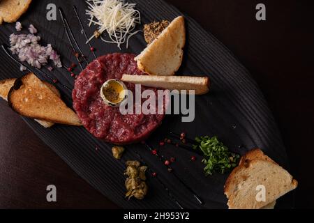 Tartare di manzo con uovo di quaglia e pane bianco tostato su un elegante piatto nero Foto Stock