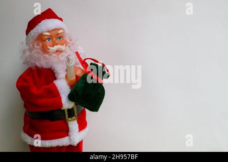 Babbo Natale con cappello rosso, borsa verde piena di regali e candele, giocattolo Babbo Natale su sfondo bianco, buon Natale decorazione, carta di Capodanno Foto Stock