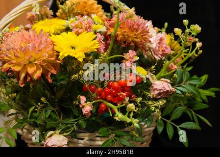 Primo piano di un bouquet di bellissimi fiori e bacche rosse in un cestino di vimini Foto Stock