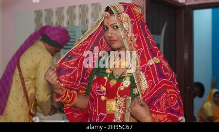 21 novembre 2021 Reengus, Rajasthan, India. Rajasthani giovane donna in costume rosso con gioielli tradizionali e bracciali colorati. Foto Stock