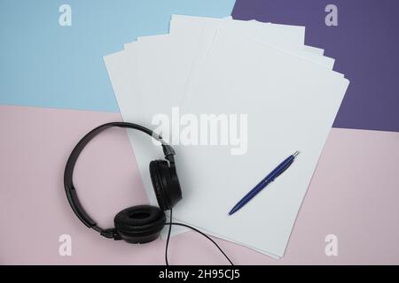 Carta, penna e cuffie vuote su sfondo di carta colorato con spazio per la copia Foto Stock