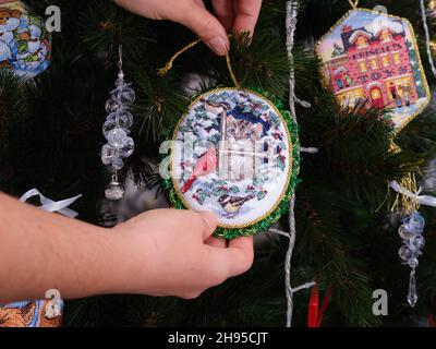 Tambov, Federazione russa - 02 dicembre 2021 Una donna che appende un ornamento a croce cucito su un albero di natale. Questo ornamento Kitten che guarda gli uccelli T Foto Stock