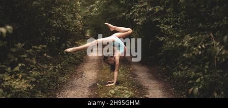 Bella ragazza giovane donna esegue esercizi di ginnastica acrobatica in una foresta. Paesaggio naturale incredibile. Foto di alta qualità Foto Stock