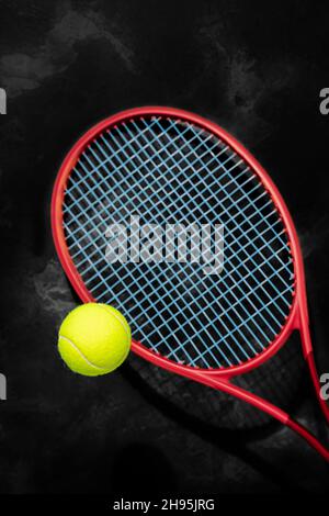 Tennis. Messa a fuoco selezionata, composizione sportiva con pallina da tennis gialla e racchetta rossa su sfondo nero testurizzato. Il concetto di gare di tennis Foto Stock