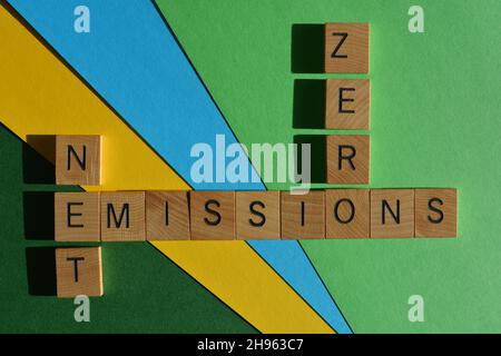 Emissioni nette zero, parole in lettere in legno in forma di parola incrociata isolate su sfondo blu verde e giallo Foto Stock