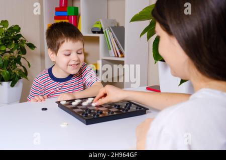 Madre e figlio giocano a dama in casa. Giochi da tavolo per bambini e bambini Foto Stock