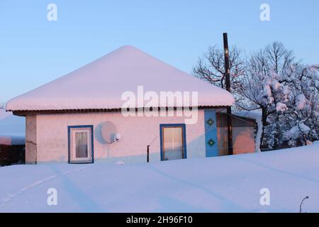 Vecchia casa di villaggio coperta di neve. Spesso strato di neve sul tetto. Foto Stock