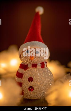 Primo piano della statuetta di Natale con un cappello Babbo Natale e sciarpa rossa e bianca con fata d'oro sfocata sullo sfondo Foto Stock