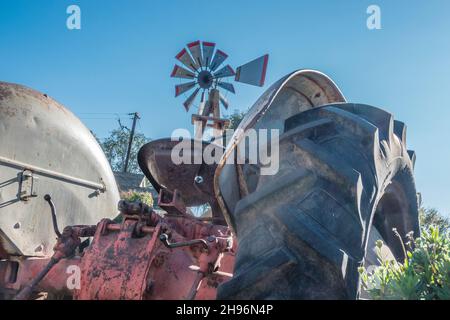 Un dettaglio di trattore antico con un vecchio mulino a vento sullo sfondo a Goleta, California. Foto Stock