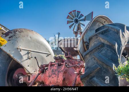 Un dettaglio di trattore antico con un vecchio mulino a vento sullo sfondo a Goleta, California. Foto Stock