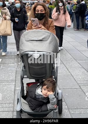 Mamma con i bambini in stow in un passeggino sul suo telefono a piedi a Times Square il Black Friday 2021 con la pandemia di Covid-19 ancora con noi a New York City. Foto Stock