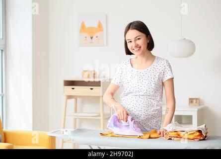 Giovane donna incinta che stira il bodysuit del bambino a casa Foto Stock