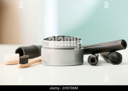 Vaso con polvere di dente di carbone attivo, spazzole e bastoni di bambù sul tavolo Foto Stock