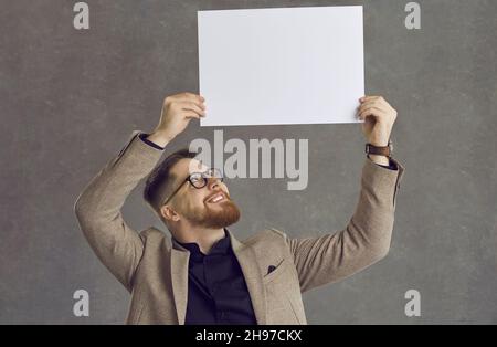 Ritratto di studio di un giovane uomo d'affari felice che tiene una carta bianca mockup banner Foto Stock