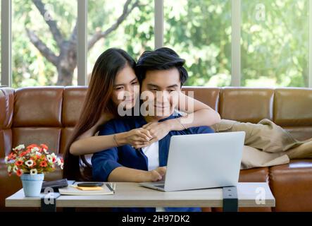 I giovani amanti trascorrono insieme le vacanze in soggiorno. Entrambi sono interessati alle informazioni sui prodotti internet mentre l'uomo che digita il tasto Foto Stock