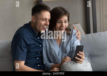 Felice scioccato coppia di incontri millennial che staring allo schermo dello smartphone Foto Stock