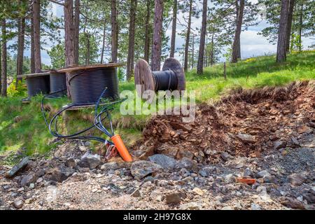 Il cavo elettrico ad alta tensione e i tubi dell'acqua sono disposti in una trincea piena di pietre. Bobina di cavo, bobina di legno di cavo elettrico. Foto Stock