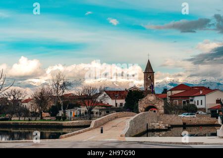 Ponte sul canale e ingresso alla storica città di Nin, Croazia. Vette innevate del monte Velebit. Bellissimo paesaggio. Foto Stock