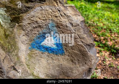 Escursioni blu triangolo vernice marcatura su una roccia con escursionista sul sentiero. Foto Stock