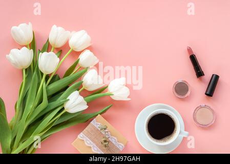 Tazza di caffè, confezione regalo, attrezzi per il trucco, cosmetici e bouquet di tulipani su sfondo rosa, vista dall'alto. Giorno della donna o concetto di giorno della madre. Creativa Foto Stock