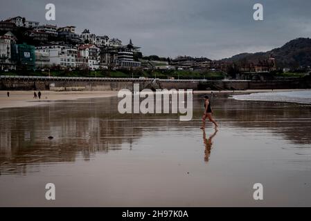 A Donostia un nuotatore cammina lungo la spiaggia di la Concha durante la bassa marea di prima mattina. Foto Stock