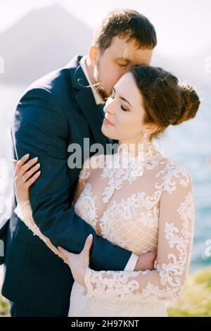 Lo sposo abbraccia la sposa e la bacia. Vista laterale. Primo piano Foto Stock