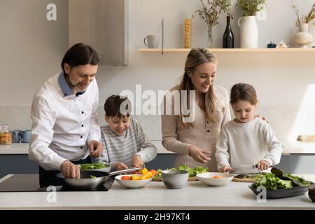 Felici genitori che cucinano con i bambini piccoli a casa. Foto Stock