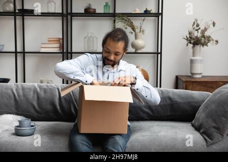 Felice uomo afroamericano disimballaggio scatola di cartone. Foto Stock