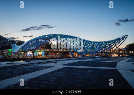 Vista panoramica del Ponte della Pace pedonale in vetro e acciaio sul fiume Mtkvari in serata. Tbilisi, Georgia. Foto Stock