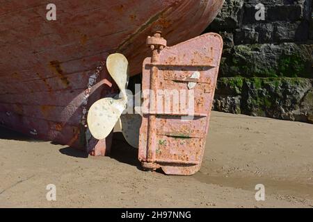 Timone e elica di una barca lasciata in alto e asciutto sulla sabbia dalla marea in declino a Barry, Galles del Sud, Regno Unito Foto Stock