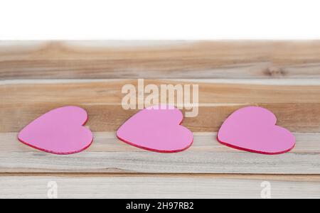 Tre cuori su una superficie di legno isolato. Cuori rosa in fila su un albero e su sfondo bianco. Foto Stock