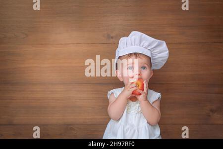 Bambino nel cappello di uno chef. Il bambino morde la mela Foto Stock