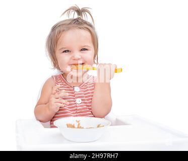 Bambino seduto in sedia e mangiare porridge con cucchiaio isolato su sfondo bianco Foto Stock