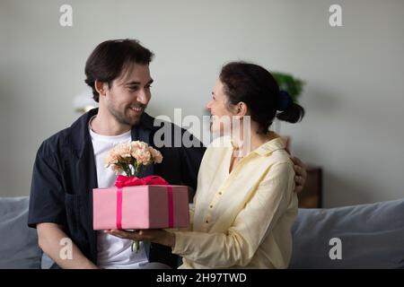 Mamma di mezza età eccitata che riceve un regalo a sorpresa e un mazzo di fiori Foto Stock