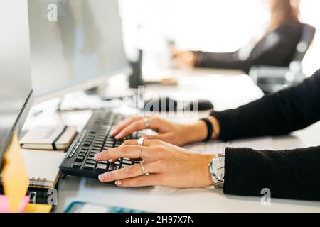 Primo piano delle mani della donna che digita un computer su una scrivania disordinata Foto Stock