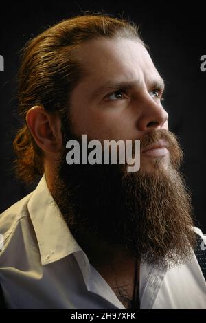 primo piano ritratto di un uomo brutale con una barba e capelli lunghi che guarda in su. Foto Stock