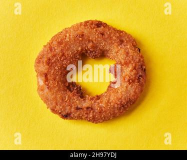 Singolo anello di cipolla impanato su sfondo giallo Foto Stock