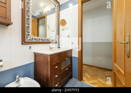 Servizi igienici con mobili vintage scuri con specchio con pavimenti in muratura e parquet nella hall Foto Stock