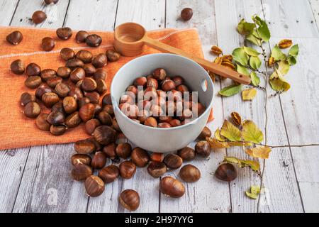 Ciotola con nocciole tostate e castagne su tavola di legno con foglie e ciotola di legno Foto Stock