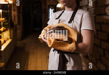 Una donna tiene nelle sue mani un pane rotondo scuro appena sfornato. Foto Stock