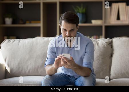 Un uomo millennial focalizzato un casual utilizzando il cellulare sul divano Foto Stock