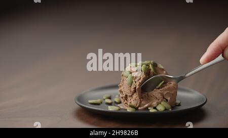 uomo mangiare gelato al cioccolato con semi di punpkin su piattino su tavola di legno, foto ampia Foto Stock